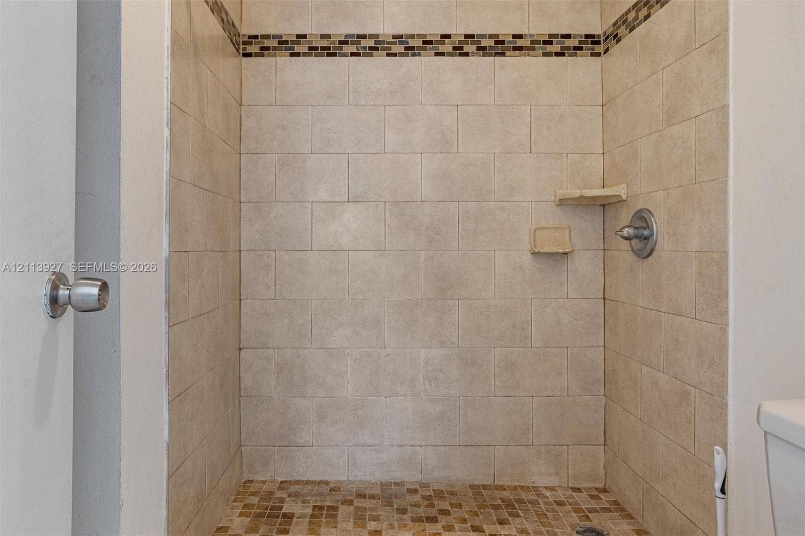 4900 NW 79th Avenue, #202, Doral, Doral, FL 33166 Walk-in shower featuring neutral rectangular wall tile, mosaic tile accent border, integrated corner shelving, and brushed nickel hardware