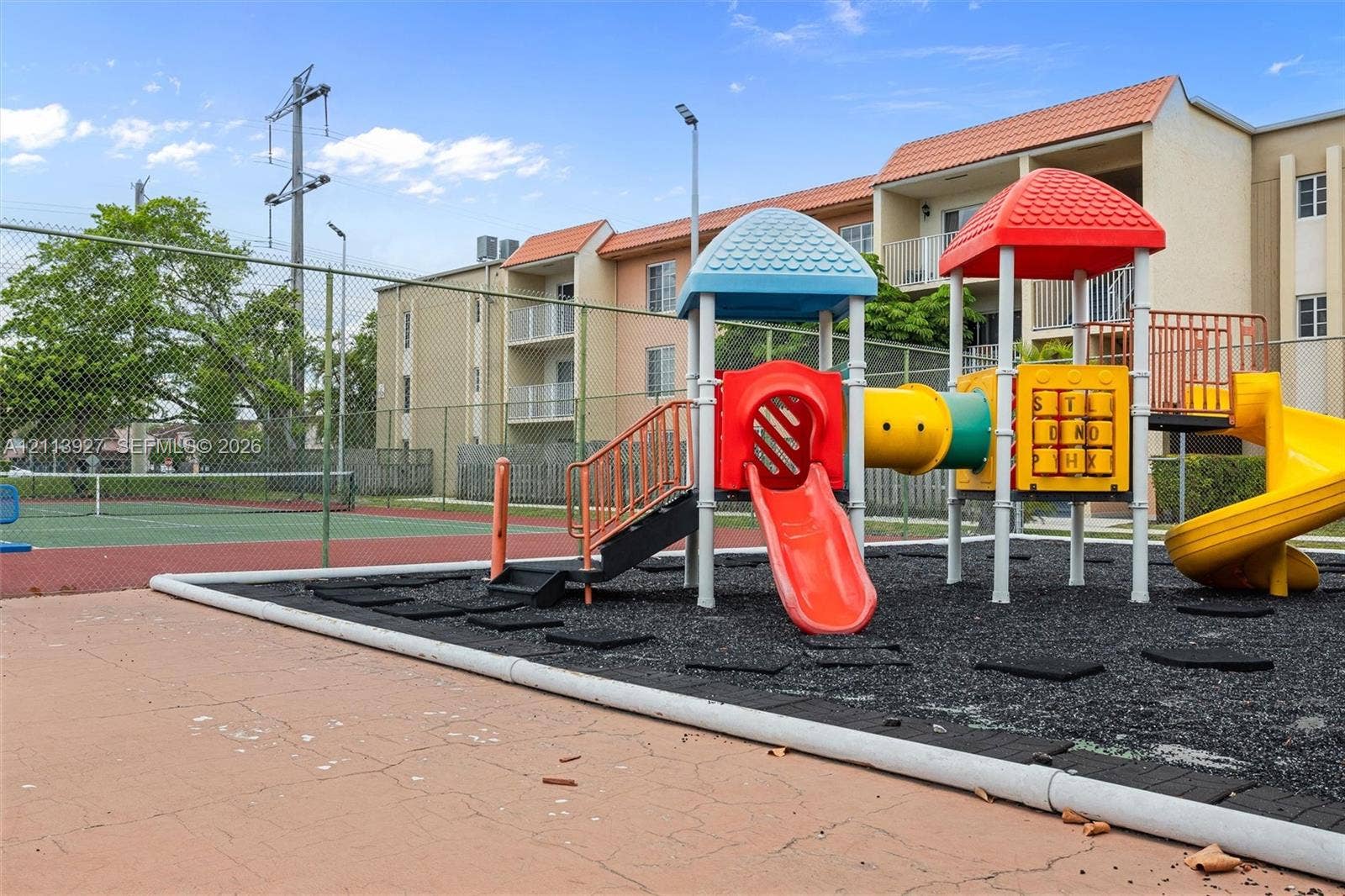 4900 NW 79th Avenue, #202, Doral, Doral, FL 33166 Playground area featuring a multi-tiered structure with a slide, hard-surfaced tennis court, and perimeter chain-link fencing