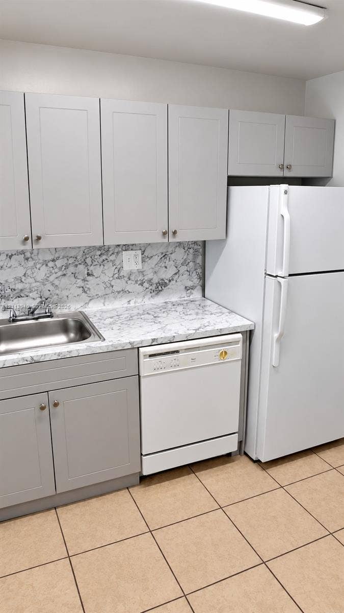 11150 SW 196th Street, #D211, Cutler Bay, Cutler Bay, FL 33157 Shaker-style cabinetry in a neutral finish, stone-patterned laminate countertop, stainless steel sink with dual-handle faucet, integrated dishwasher, and ceramic tile flooring