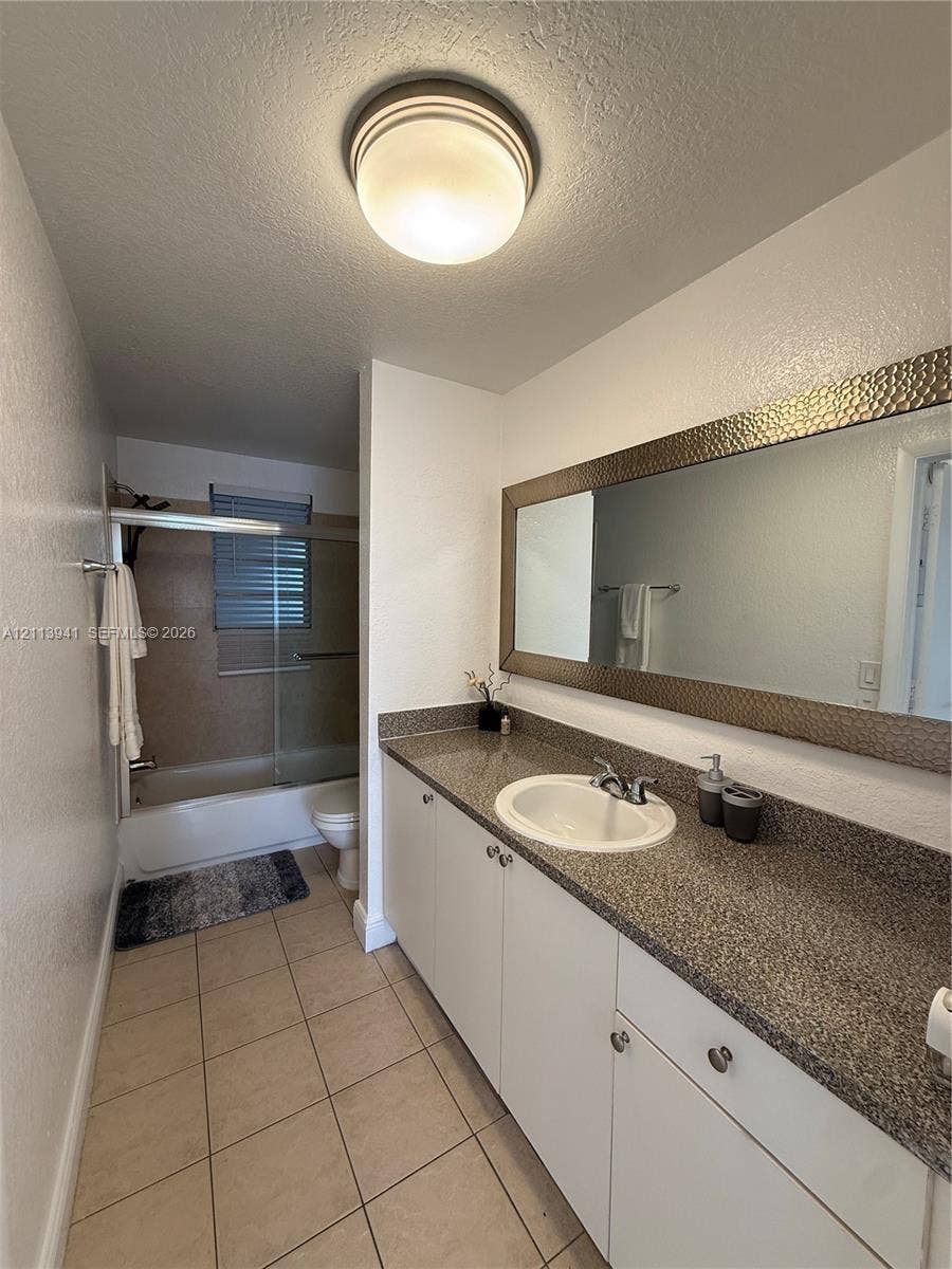 17255 SW 95th Avenue, #457, Palmetto Bay, Palmetto Bay, FL 33157 Full-width vanity with solid-surface countertop, integrated basin, tiled flooring, large framed wall mirror, and glass-enclosed shower and tub combination