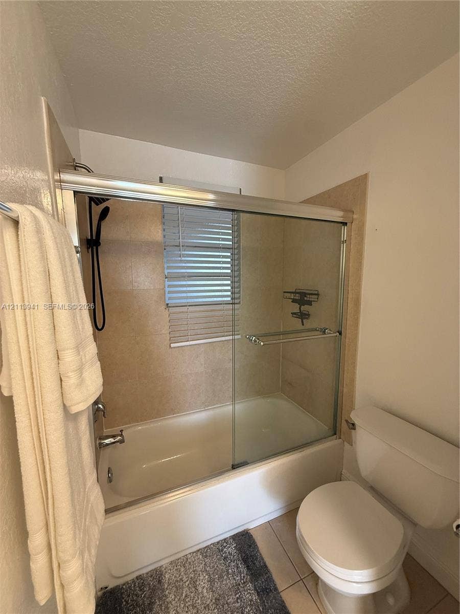 17255 SW 95th Avenue, #457, Palmetto Bay, Palmetto Bay, FL 33157 Bathtub with glass sliding doors, neutral tile surround, black handheld shower fixture, and tiled flooring