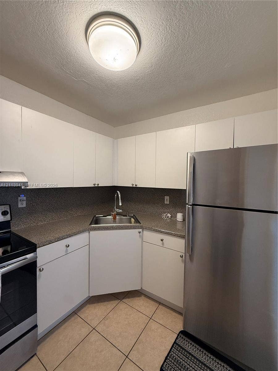 17255 SW 95th Avenue, #457, Palmetto Bay, Palmetto Bay, FL 33157 Kitchen featuring white cabinetry, speckled stone-finish countertops, stainless steel appliances, corner-mounted sink, and neutral tile flooring