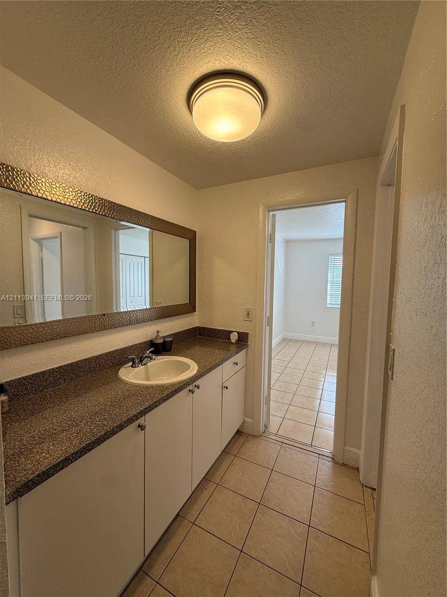 17255 SW 95th Avenue, #457, Palmetto Bay, Palmetto Bay, FL 33157 Extended vanity featuring a speckled stone-finish countertop, white cabinetry, a circular undermount sink, and a full-width mirror with a hammered metal-finish frame, complemented by ceramic tile flooring