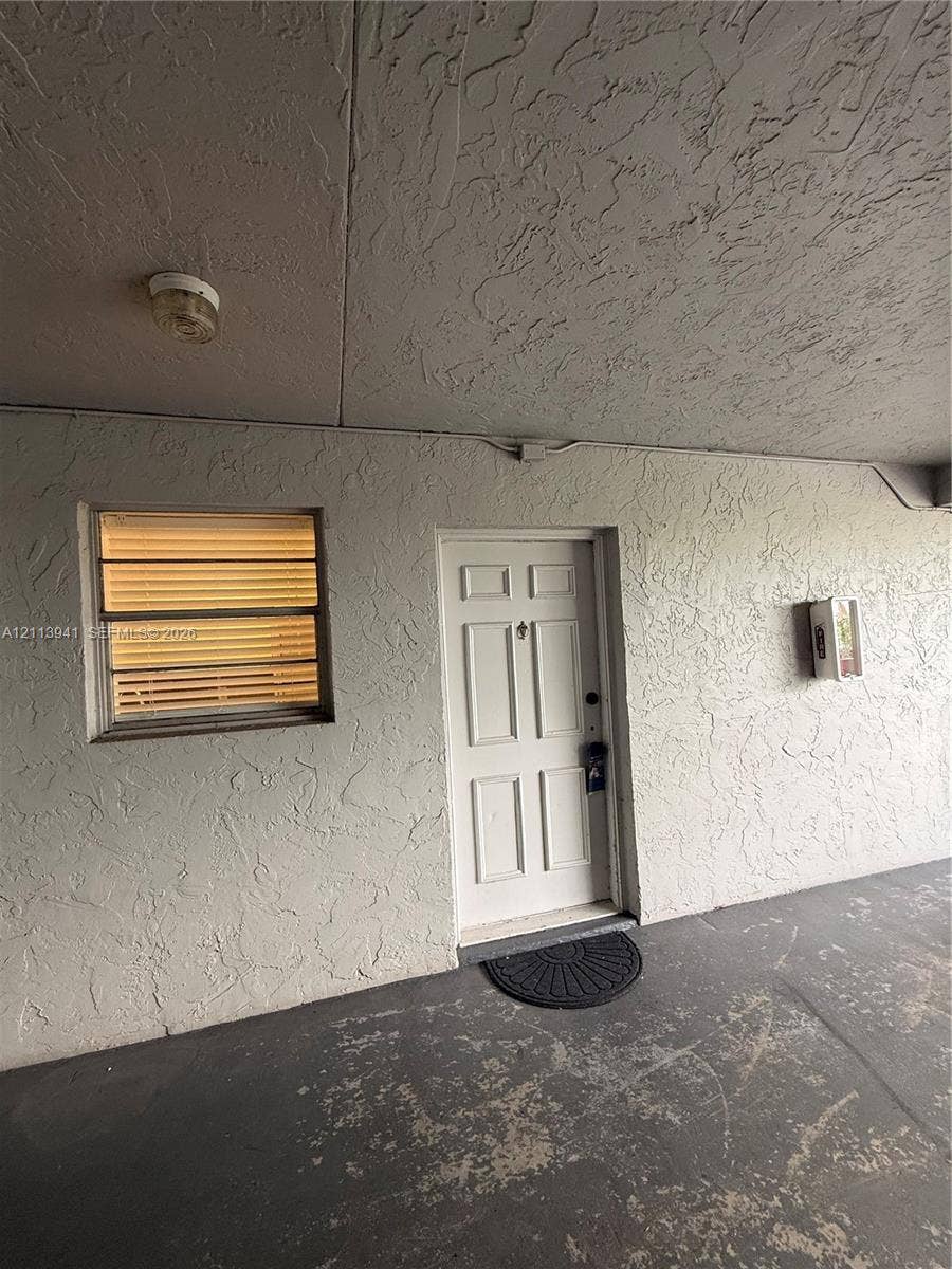 17255 SW 95th Avenue, #457, Palmetto Bay, Palmetto Bay, FL 33157 Covered exterior entryway featuring textured stucco walls, a six-panel entry door, jalousie window, and flush-mount ceiling lighting