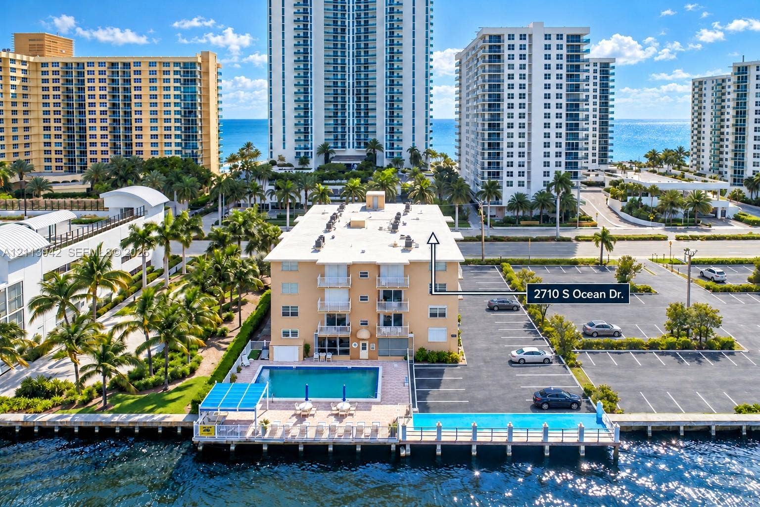 2710 S Ocean Drive, #401, Hollywood, FL 33019 Waterfront mid-rise building featuring a ground-level swimming pool, expansive paved parking area, private dockage, and manicured palm tree landscaping