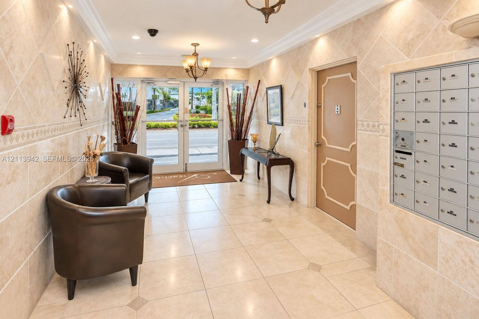 2710 S Ocean Drive, #401, Hollywood, FL 33019 Lobby entrance featuring large-format tile flooring with decorative inserts, floor-to-ceiling stone wall cladding, built-in recessed parcel and mailboxes, and multi-light hanging chandeliers