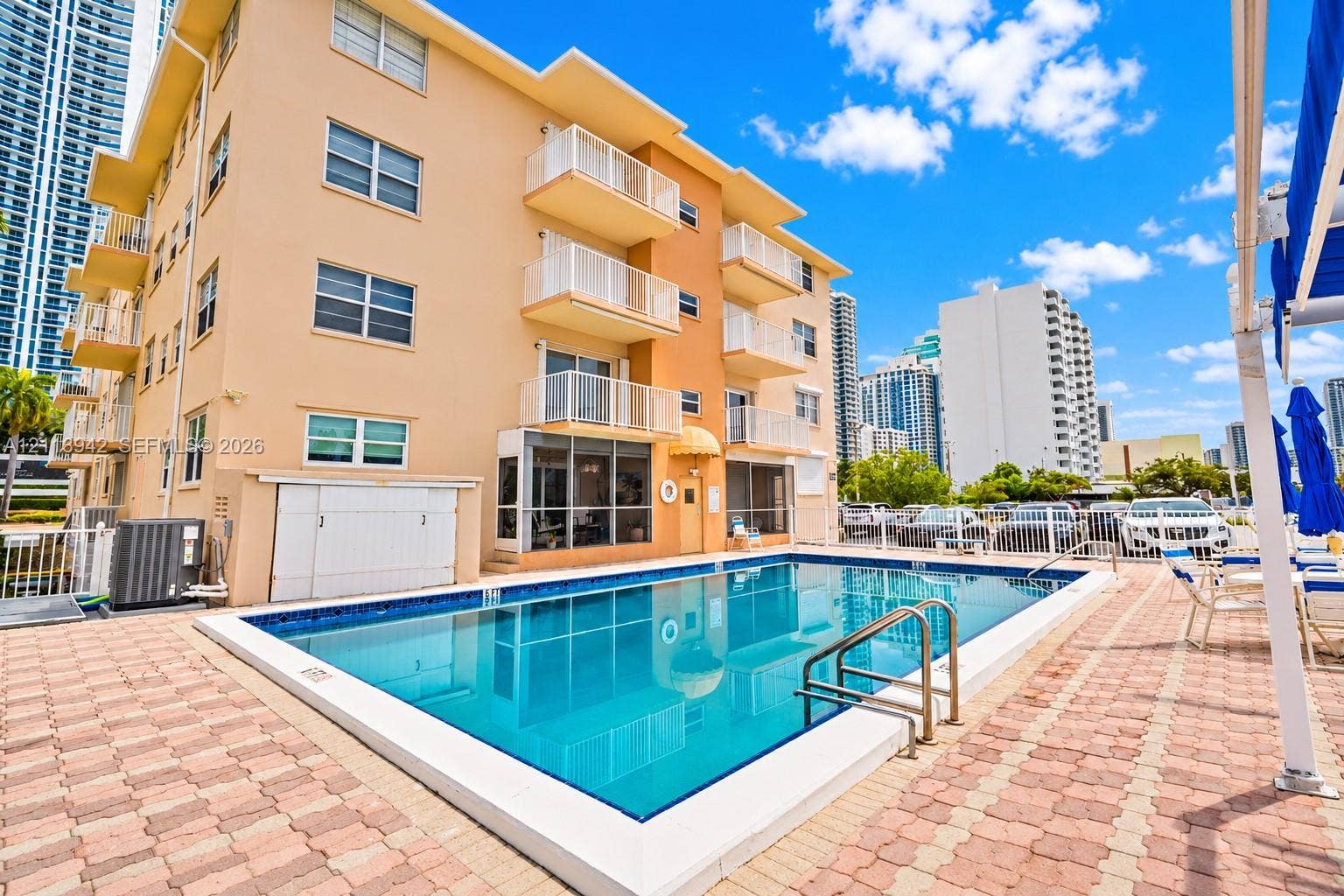 2710 S Ocean Drive, #401, Hollywood, FL 33019 Rectangular swimming pool with tiled coping, surrounded by a brick paver deck, featuring multi-story building exterior with private balconies and glass-enclosed ground level space