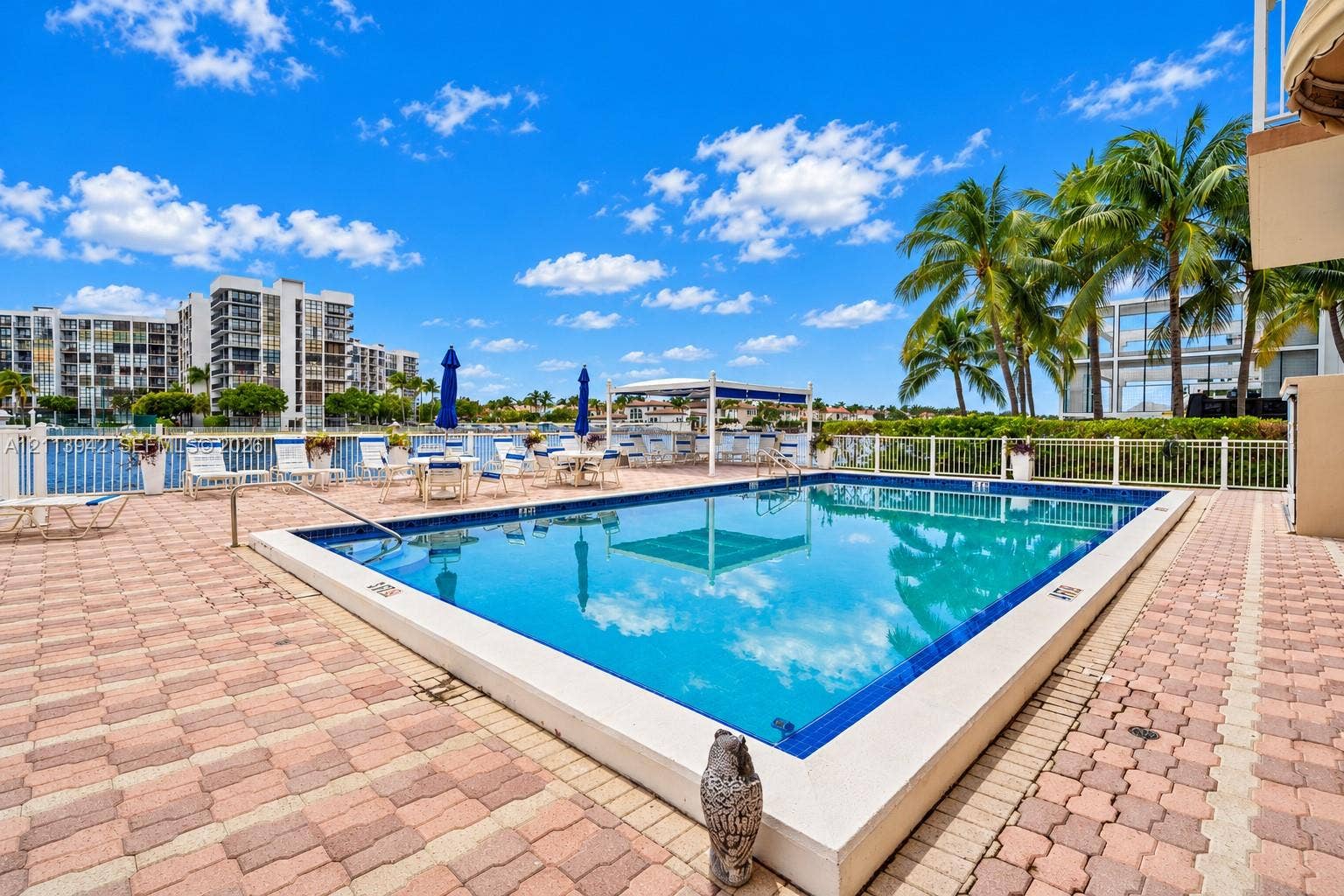 2710 S Ocean Drive, #401, Hollywood, FL 33019 In-ground swimming pool with tile border, brick paver decking, white perimeter fencing, and mature palm trees