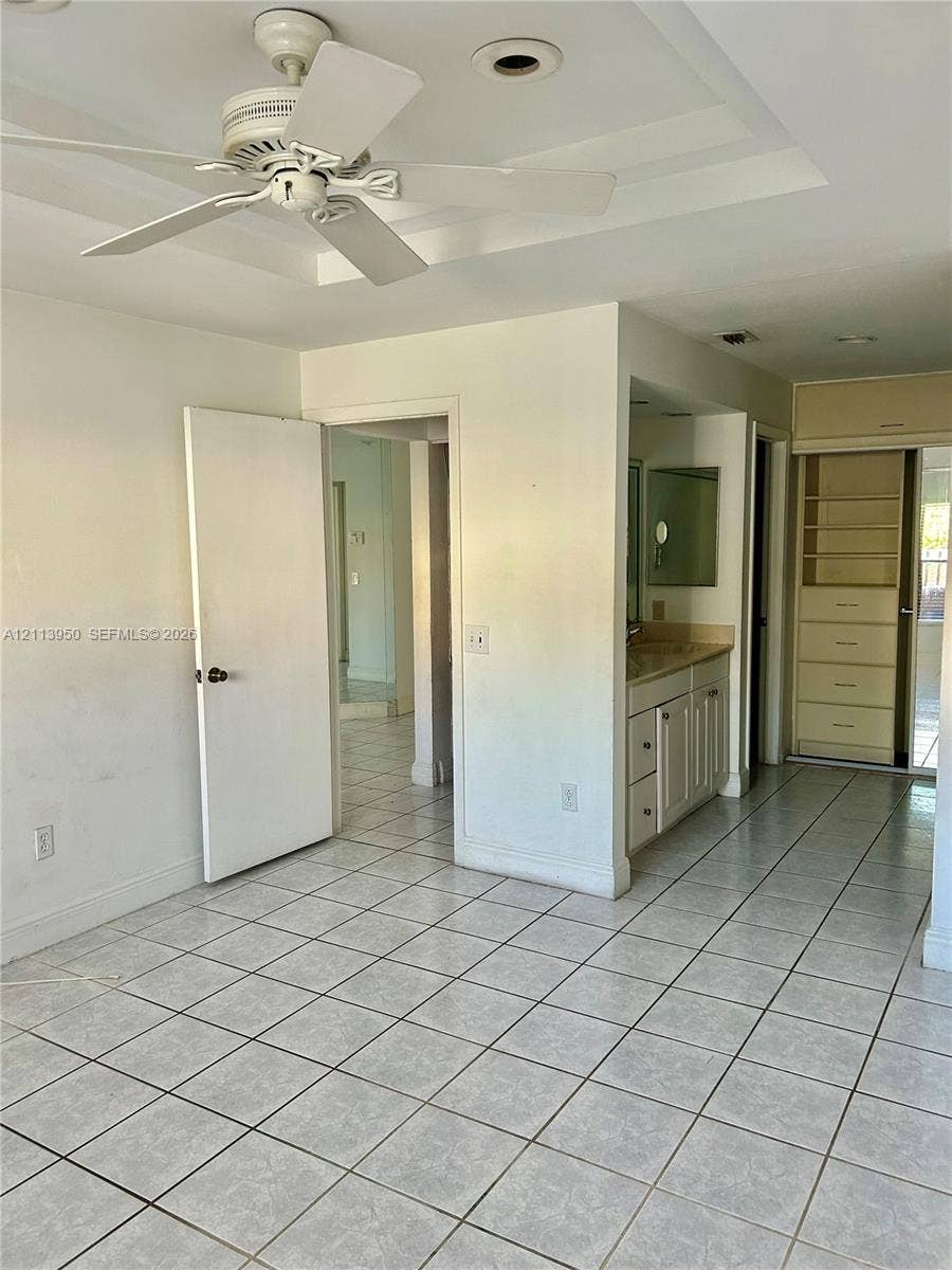 Tiled flooring, ceiling fan, vanity with cabinetry, and built-in shelving unit
