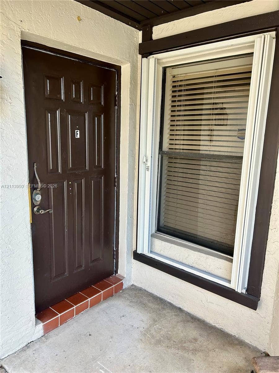 Exterior entry featuring a six-panel door, metal hardware, terracotta-tiled threshold, and window with white trim