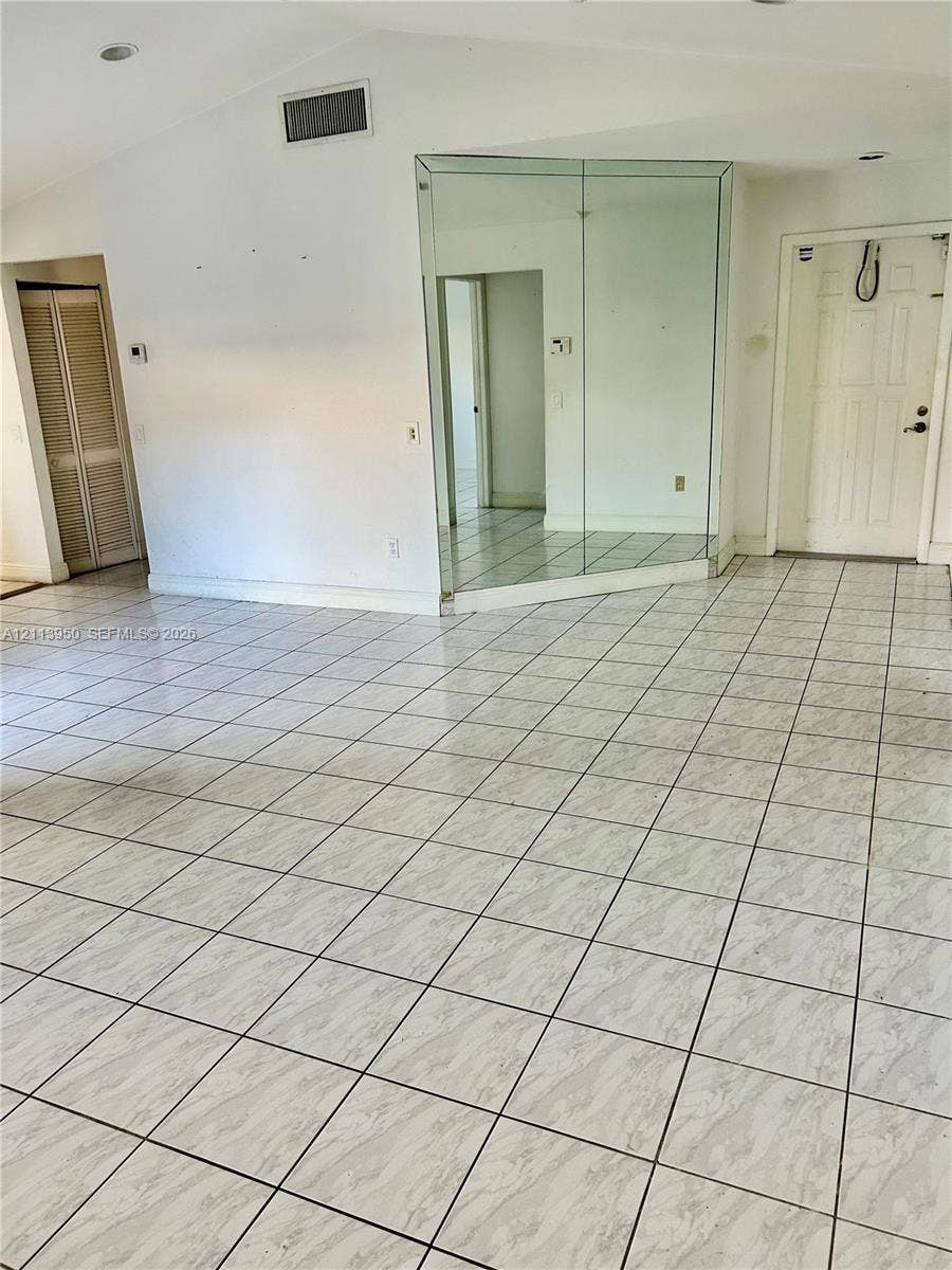 Vaulted ceilings with recessed lighting, large-format tiled flooring, floor-to-ceiling mirrored wall paneling, and bi-fold closet doors
