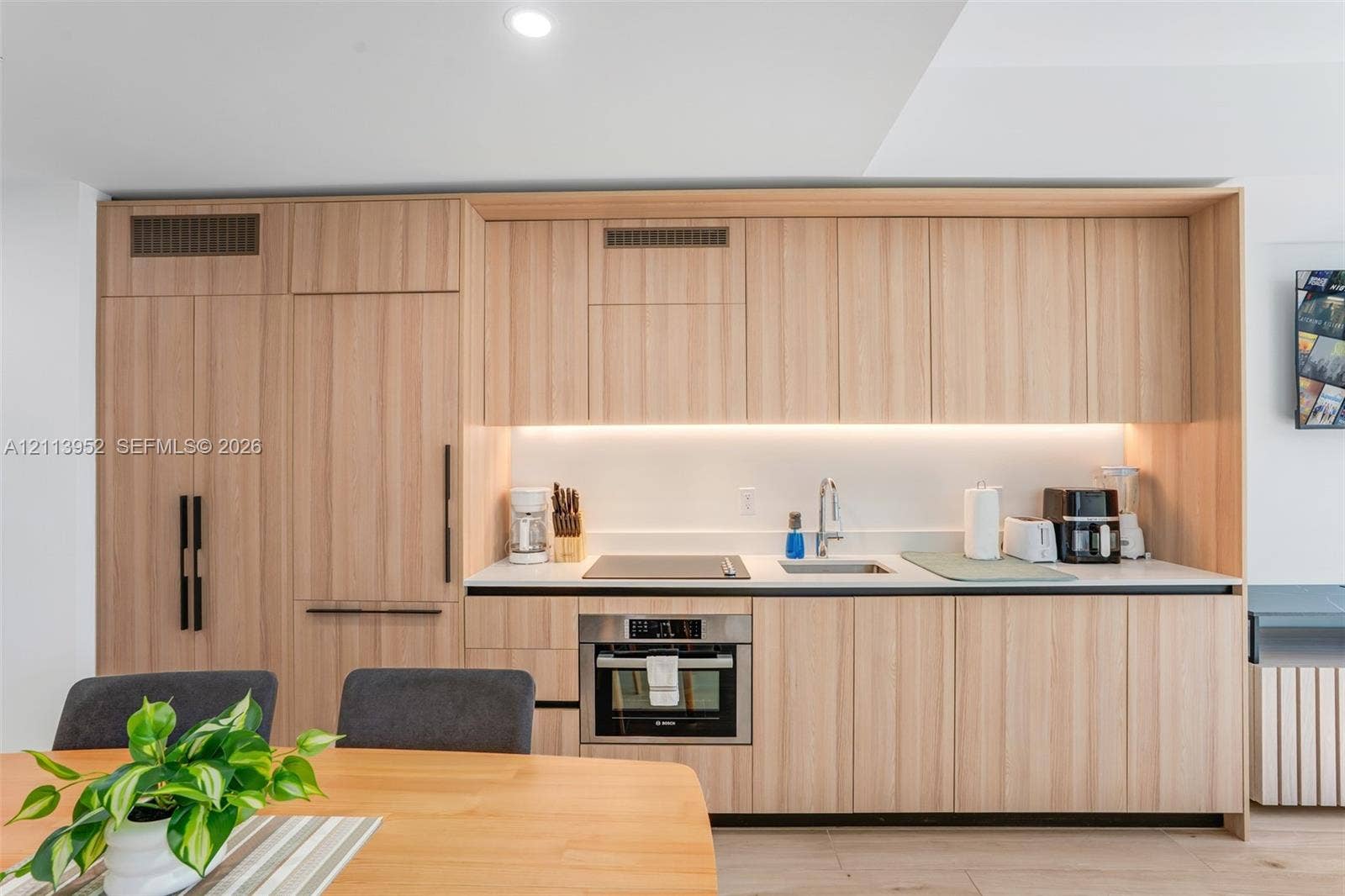 Modern kitchen featuring flat-panel wood-finish cabinetry, integrated panel-ready appliances, quartz countertops, undermount sink with gooseneck faucet, and under-cabinet LED lighting
