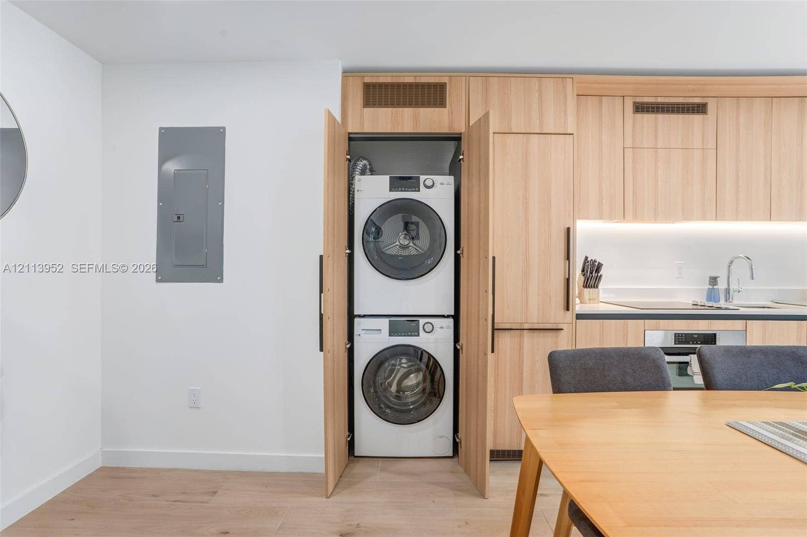 Built-in stacked laundry closet with wood-finish cabinetry, integrated cabinetry, light-toned wood-finish flooring, and recessed under-cabinet lighting