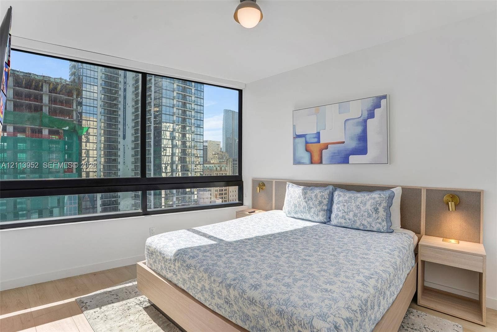 Floor-to-ceiling windows, integrated wood-finish headboard with built-in side tables, recessed ceiling light, and light wood-finish flooring