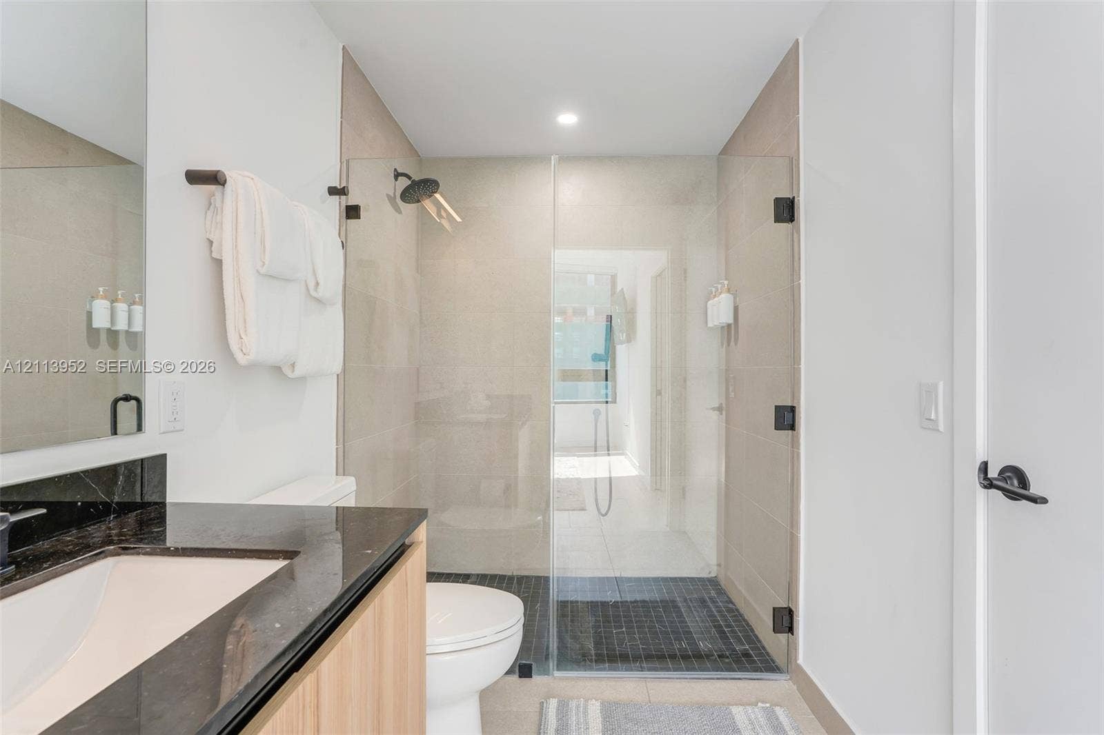 Bathroom featuring a vanity with a dark stone countertop, an integrated sink, a glass-enclosed walk-in shower with neutral wall tile, and matte black hardware