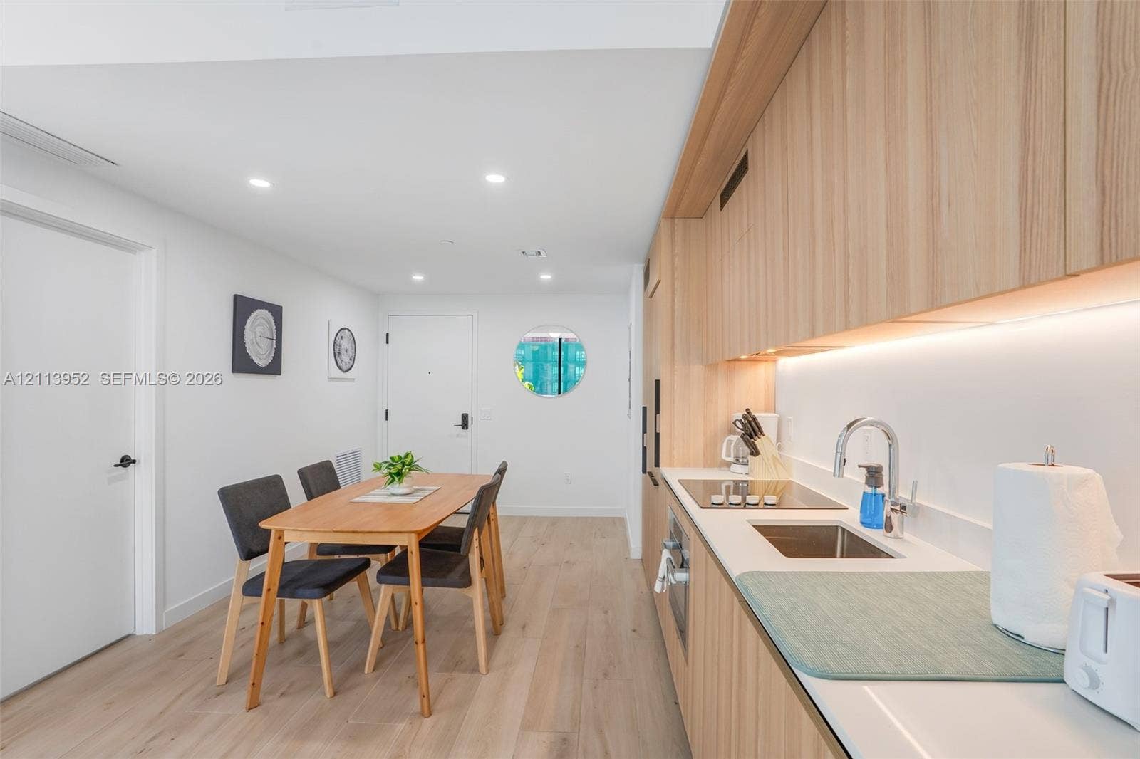 Kitchen featuring light wood-finish cabinetry, white solid-surface countertops, an integrated cooktop, a stainless steel undermount sink, and recessed ceiling lighting