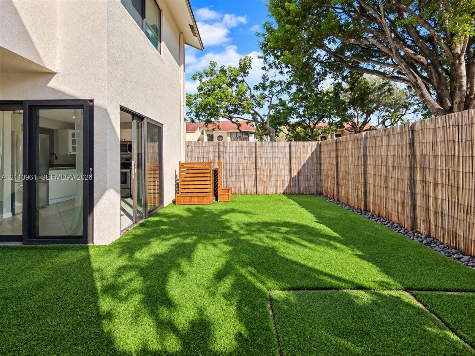 339 City View Drive, #339, Fort Lauderdale, Fort Lauderdale, FL 33311 Private fenced backyard featuring artificial turf, river rock landscaping borders, and multi-panel sliding glass doors