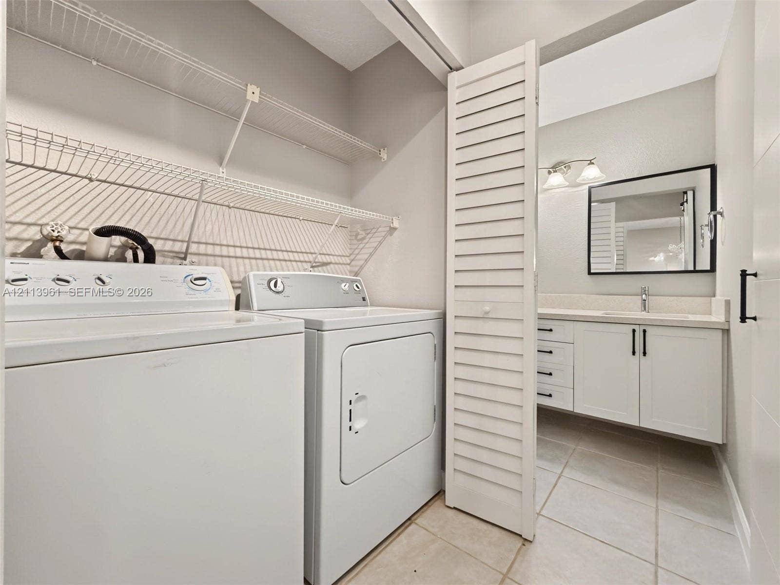 339 City View Drive, #339, Fort Lauderdale, Fort Lauderdale, FL 33311 Laundry area featuring wire shelving and white cabinetry with a vanity including a rectangular sink, stone-finish countertop, black hardware, and a framed mirror