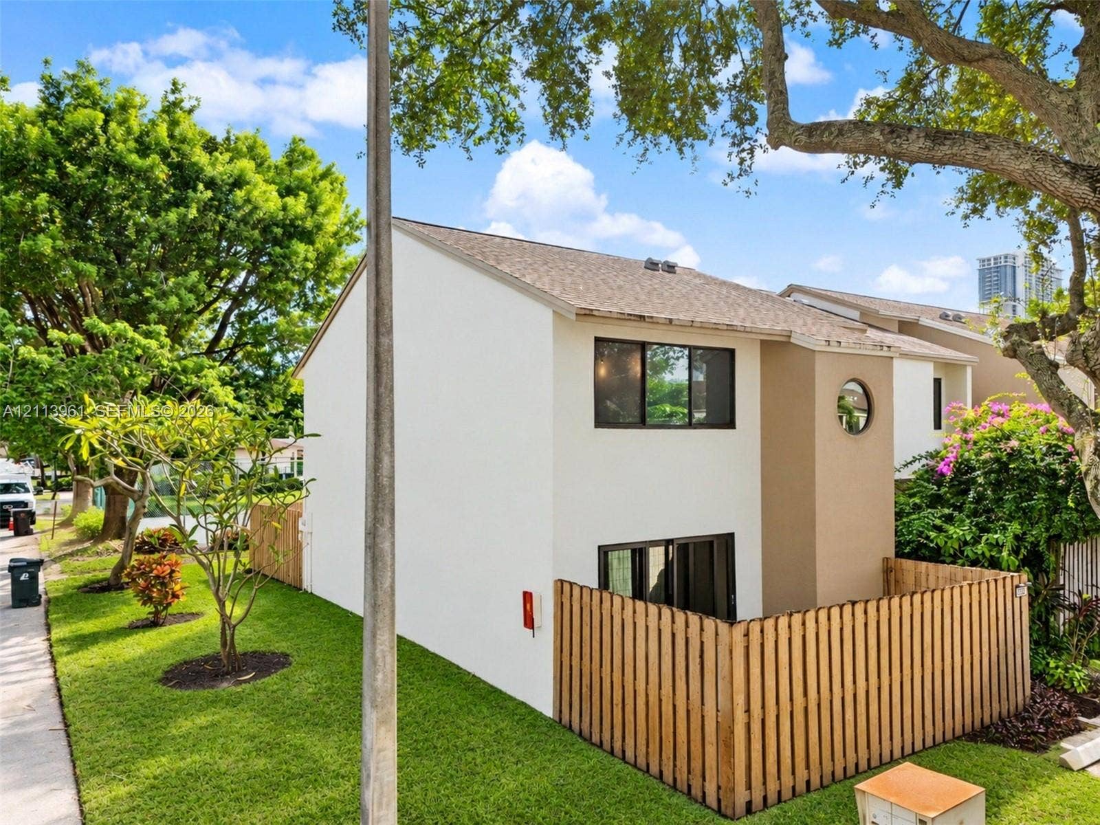 339 City View Drive, #339, Fort Lauderdale, Fort Lauderdale, FL 33311 Two-story exterior featuring a neutral-toned stucco finish, wood-plank privacy fencing, an accent circular window, and mature landscaping