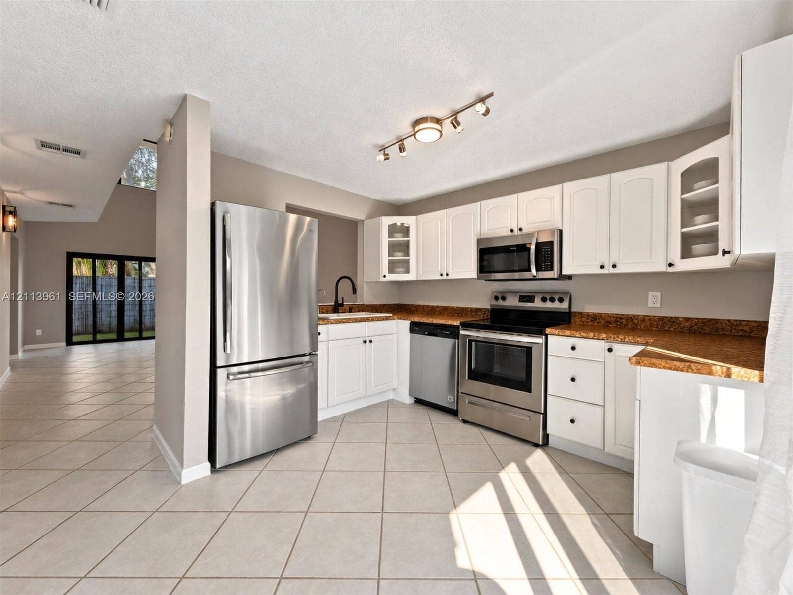 339 City View Drive, #339, Fort Lauderdale, Fort Lauderdale, FL 33311 Kitchen featuring white cabinetry with glass-panel display doors, stainless steel appliances, stone-finish countertops, ceramic tile flooring, and multi-directional track lighting