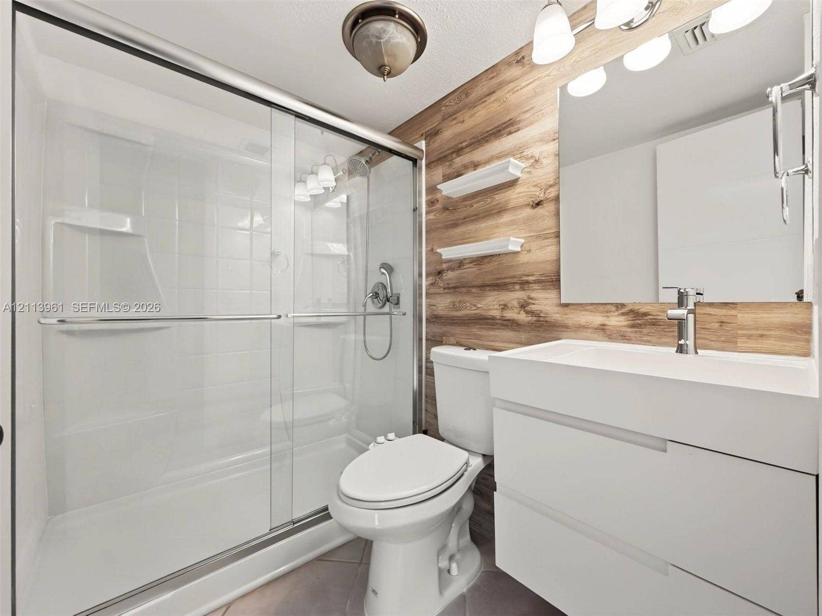 339 City View Drive, #339, Fort Lauderdale, Fort Lauderdale, FL 33311 Bathroom featuring a floating vanity with a rectangular sink, wood-finish wall paneling, a glass-enclosed shower with chrome fixtures, and built-in wall shelving