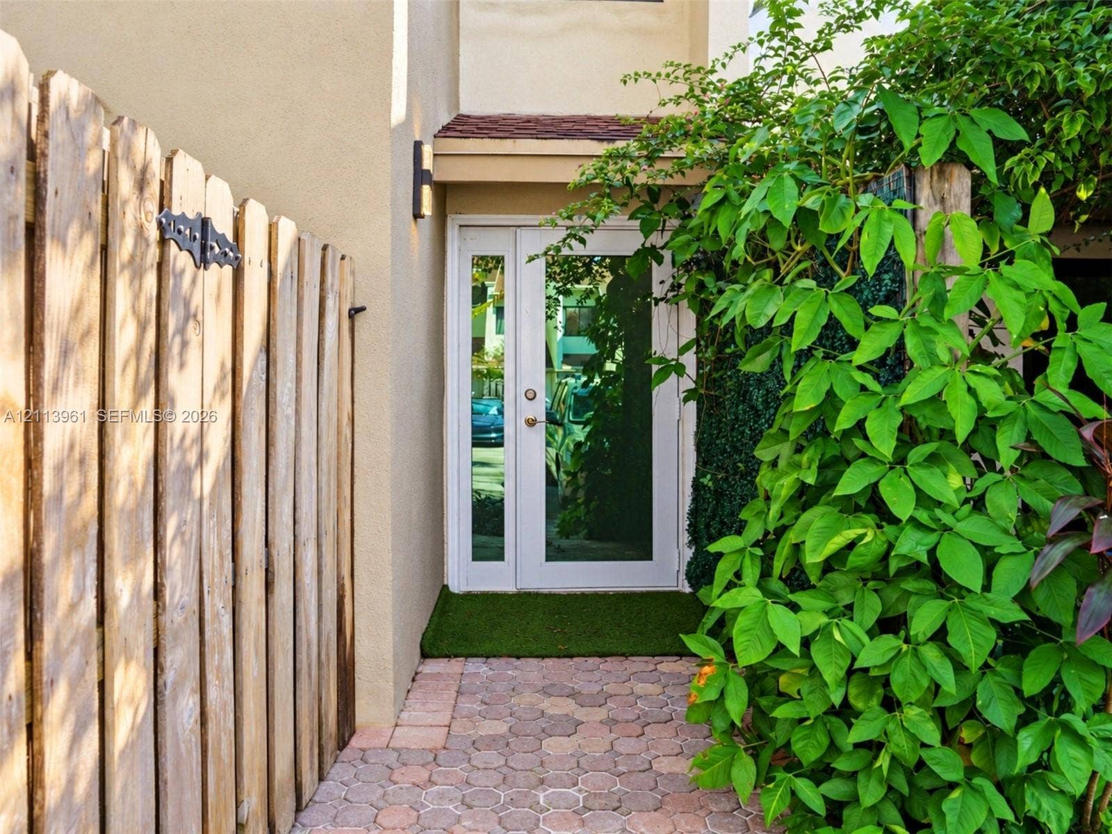 339 City View Drive, #339, Fort Lauderdale, Fort Lauderdale, FL 33311 Entrance featuring a white-frame glass door with a sidelight, geometric paver walkway, vertical wood-plank privacy fencing, and exterior wall-mounted lighting