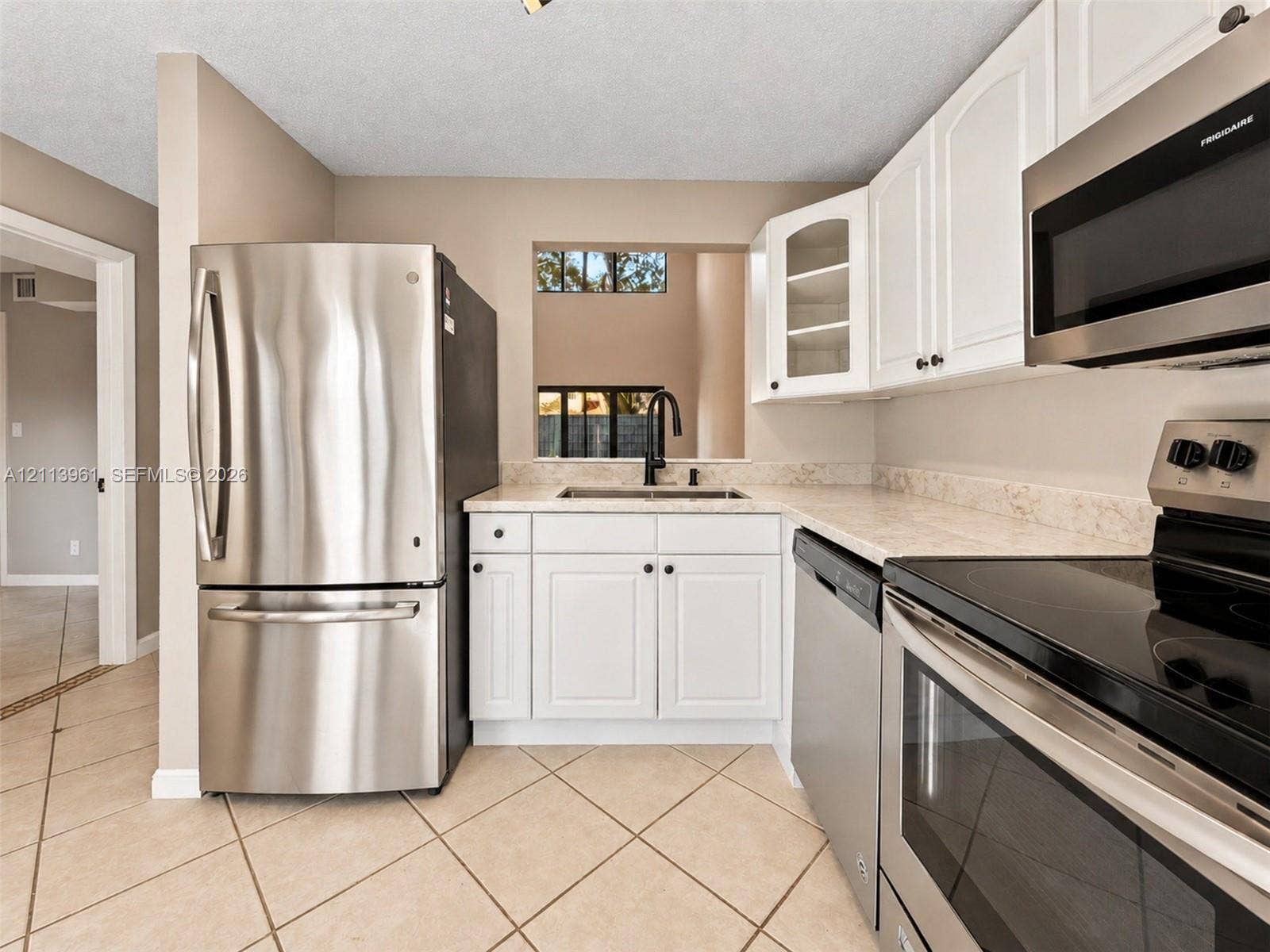 339 City View Drive, #339, Fort Lauderdale, Fort Lauderdale, FL 33311 Kitchen featuring stainless steel appliances, white cabinetry with glass-panel accents, stone-composite countertops, and neutral tile flooring