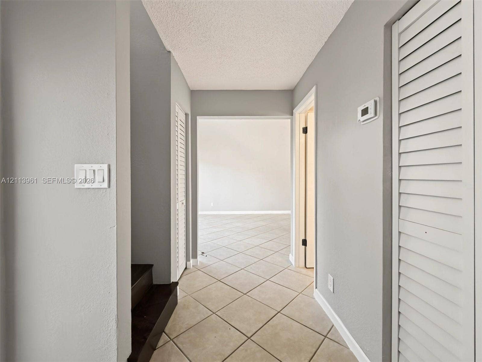 339 City View Drive, #339, Fort Lauderdale, Fort Lauderdale, FL 33311 Interior hallway featuring tile flooring laid on a diagonal, dual louvered closet doors, and dark-finished staircase treads