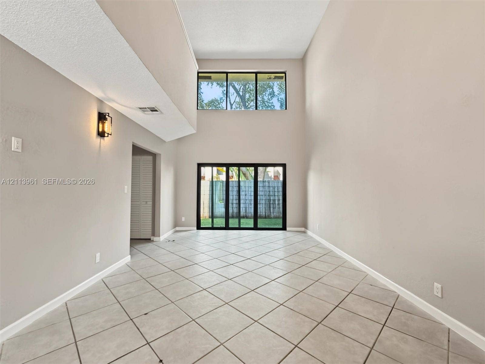 339 City View Drive, #339, Fort Lauderdale, Fort Lauderdale, FL 33311 High-ceilinged interior featuring large-format tile flooring, a multi-pane upper window, sliding glass doors, and wall-mounted sconce lighting