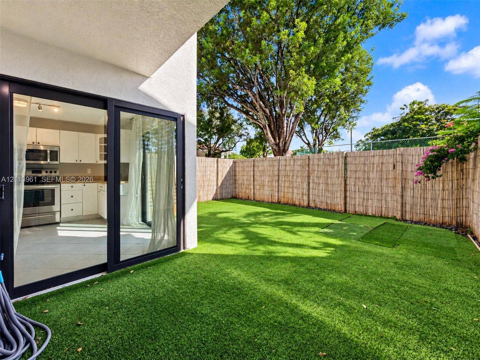 339 City View Drive, #339, Fort Lauderdale, Fort Lauderdale, FL 33311 Private backyard featuring synthetic turf, perimeter fencing, and mature trees, complemented by a covered patio with sliding glass doors