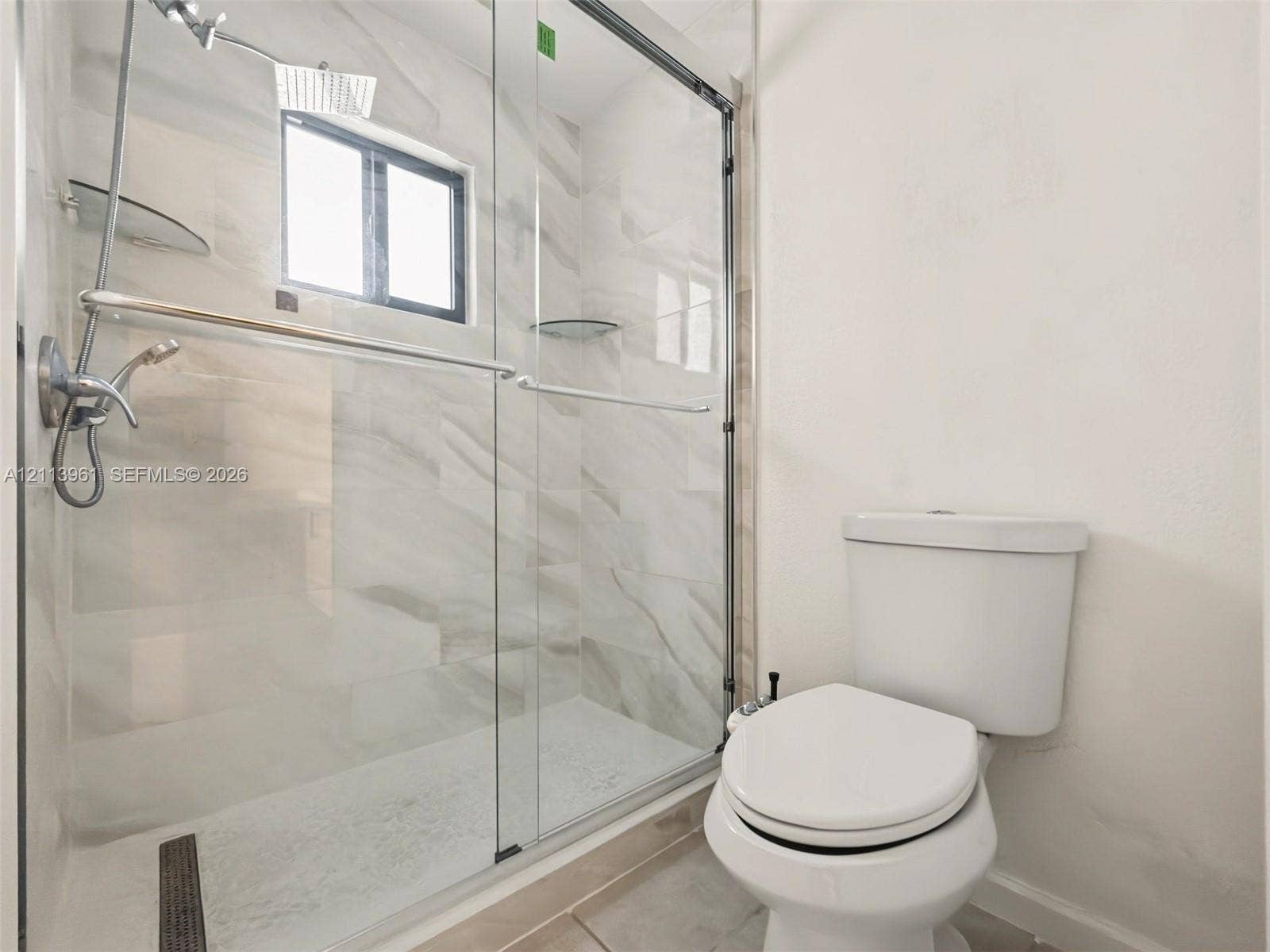 339 City View Drive, #339, Fort Lauderdale, Fort Lauderdale, FL 33311 Walk-in shower featuring a frameless glass enclosure, polished stone-finish tile surround, integrated shelving, and a dual-function chrome shower head