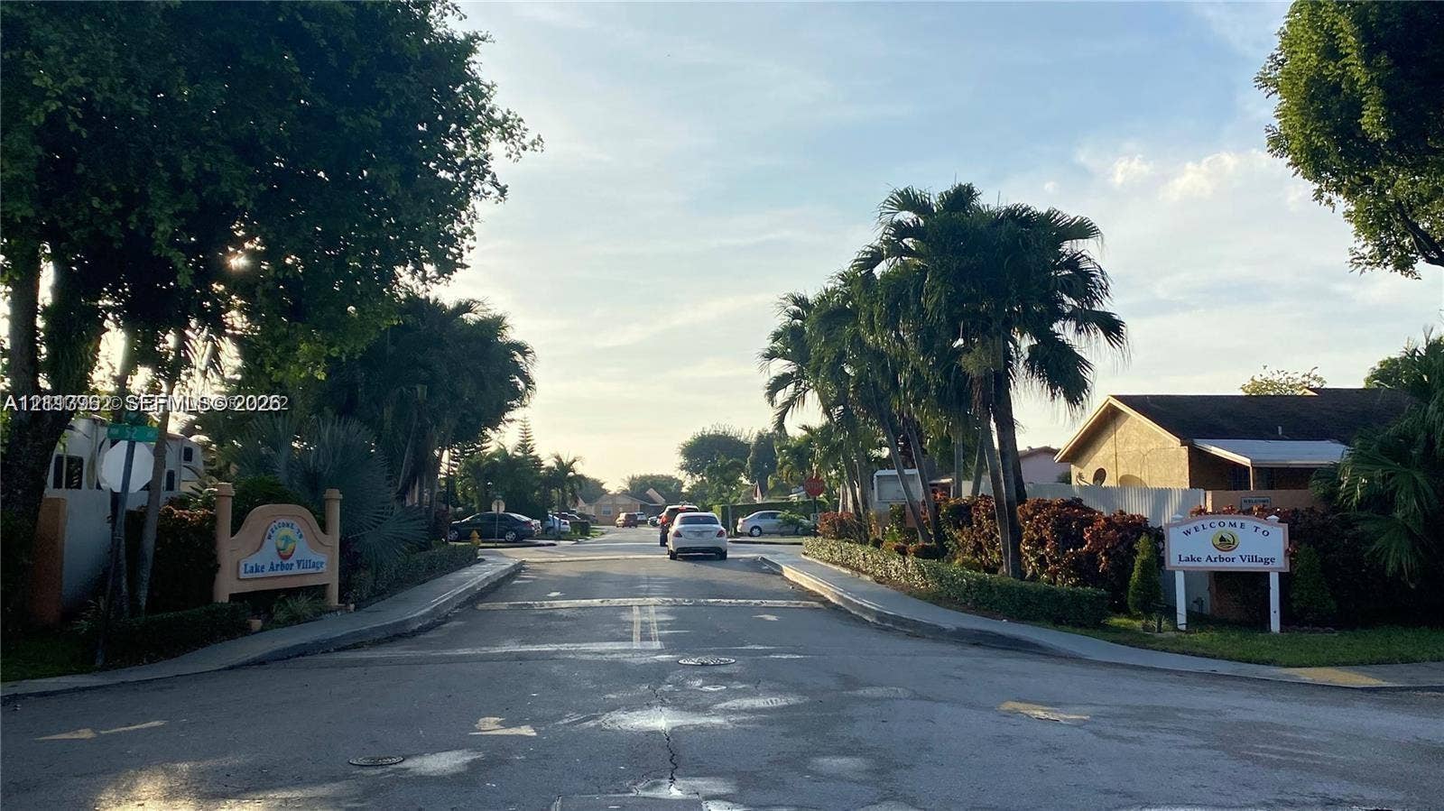 19764 NW 54 Avenue, Miami Gardens, FL 33055 Community entrance featuring paved streets, mature palm trees, decorative signage, and lush landscaping