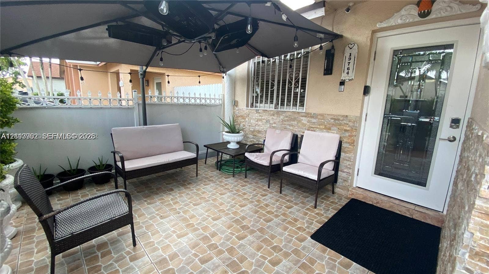19764 NW 54 Avenue, Miami Gardens, FL 33055 Covered patio featuring stone-tiled flooring, split-face stone veneer wall detailing, and a white entry door with an integrated glass panel