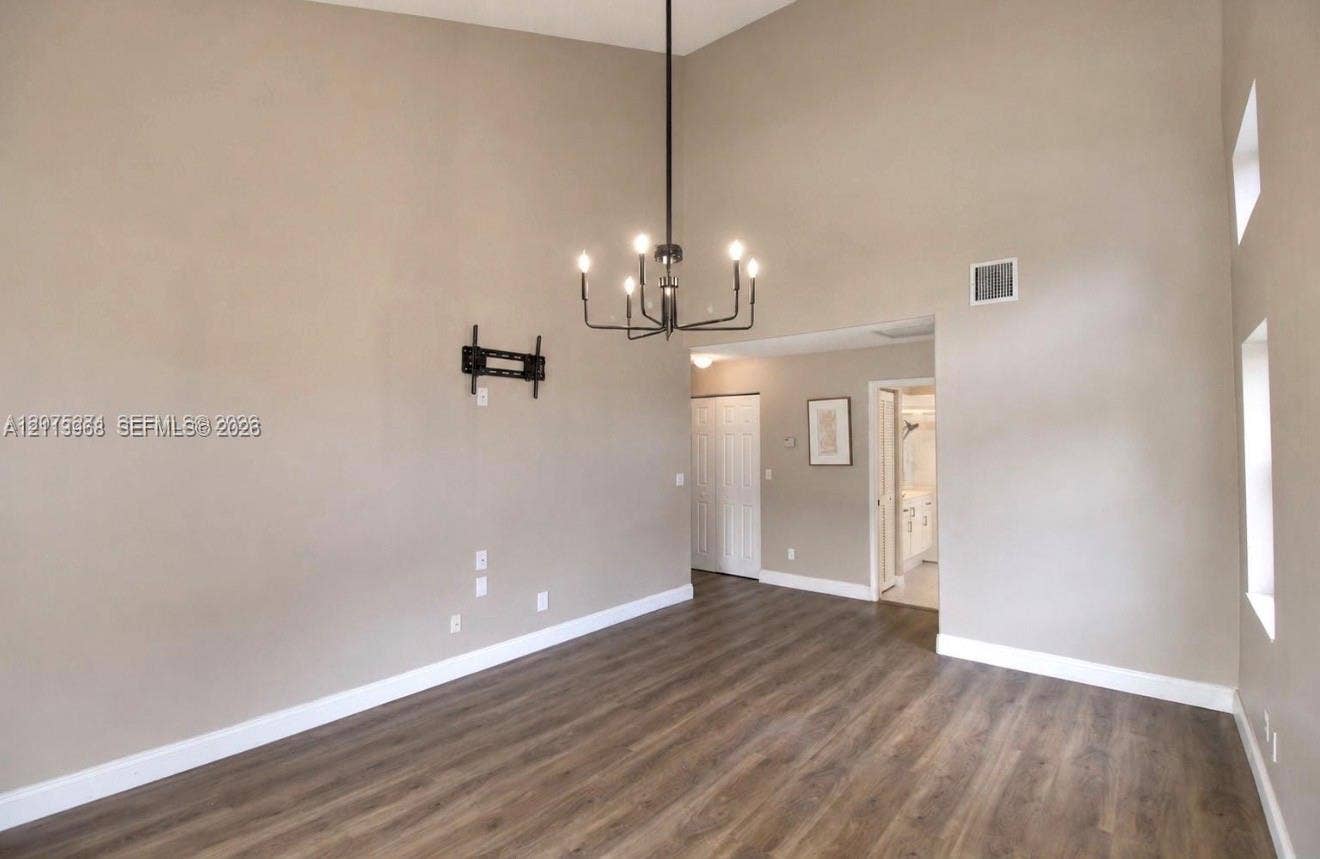 High-vaulted ceilings, dark wood-finish flooring, and a prominent six-light chandelier featuring a matte black finish