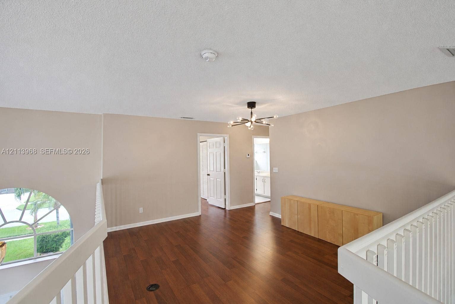Open loft area featuring wood-finish flooring, a contemporary multi-arm chandelier, an arched window with decorative muntins, and white-painted millwork railings