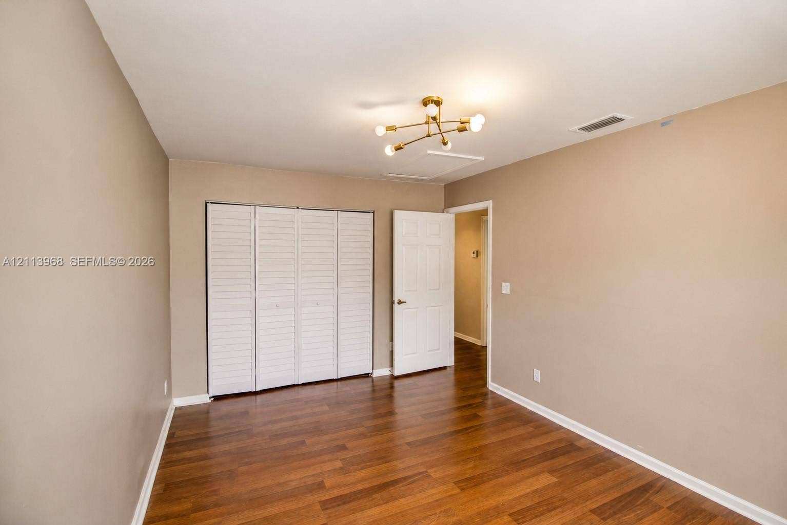 Room featuring wood-finish flooring, a multi-arm metallic light fixture, and a white six-panel door with matching bifold closet doors