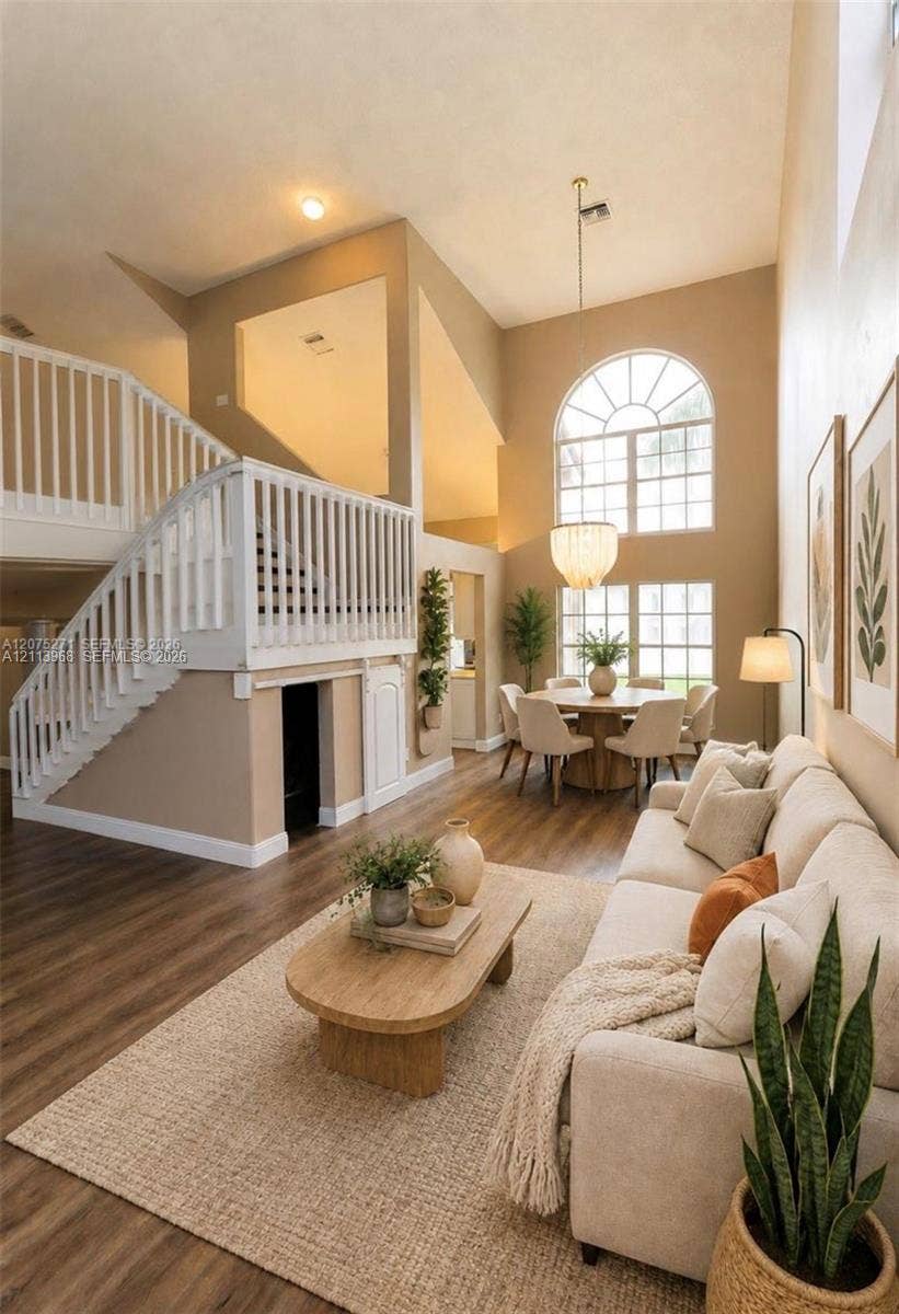 Vaulted ceilings featuring double-height windows with arched transom, wood-finish flooring, and a staircase with white vertical balusters and a built-in lower storage cabinet