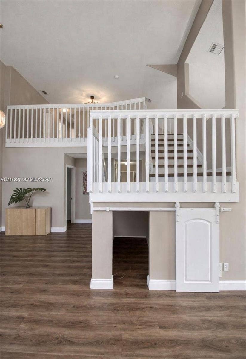 High-ceiling interior featuring wood-finish flooring, a white wooden staircase balustrade, and a lower-level built-in storage area with a sliding barn-style door
