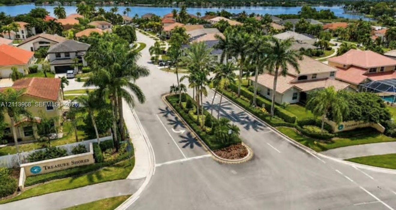 Aerial perspective of the Treasure Shores community entrance featuring a landscaped center median, palm tree-lined streets, and a waterfront position