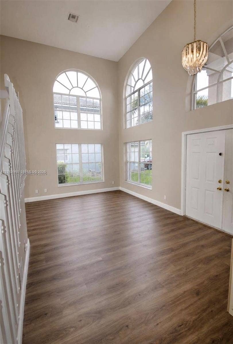 Double-height ceiling, wood-finish flooring, multi-pane arched windows, and decorative tiered pendant lighting