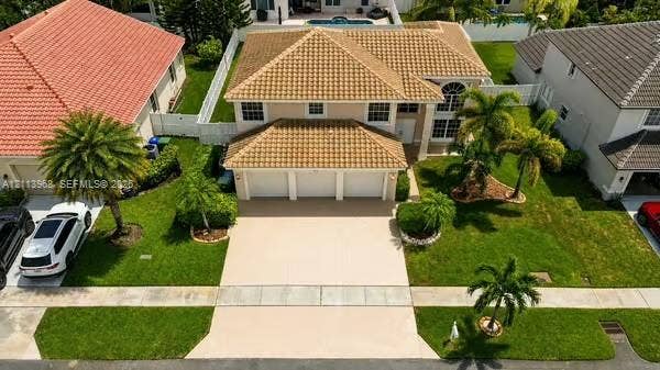 Two-story residence featuring a tile roof, three-car garage, concrete driveway, and landscaped lawn with mature palm trees
