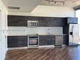 151 SE 1st Street, #1702, Miami, FL 33131 Kitchen featuring dark wood-grain cabinetry, quartz countertops, white hexagonal tile backsplash, stainless steel appliances, and exposed concrete ceilings with track lighting