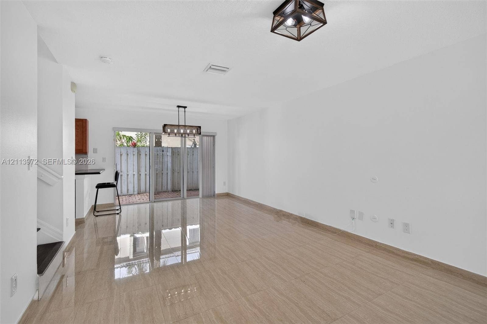 Open-concept interior featuring large-format tile flooring, modern geometric ceiling lighting, and sliding glass doors providing outdoor access