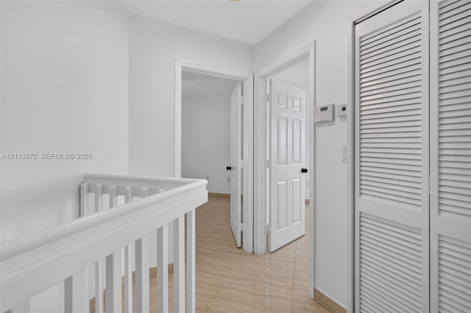 White wood-finish railings, neutral tile flooring, six-panel interior doors, and floor-to-ceiling louvered closet doors