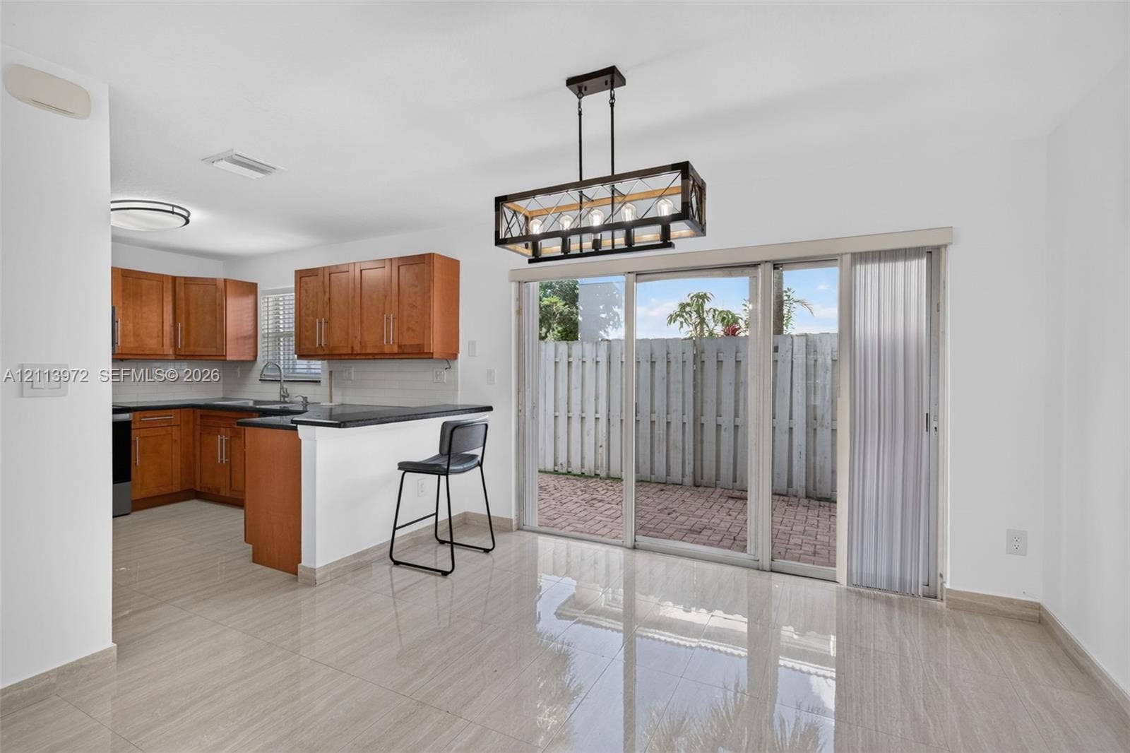 Kitchen featuring wood cabinetry, a breakfast bar with stone-finish countertops, tile flooring, a geometric multi-light chandelier, and sliding glass doors opening to a brick-paved outdoor space