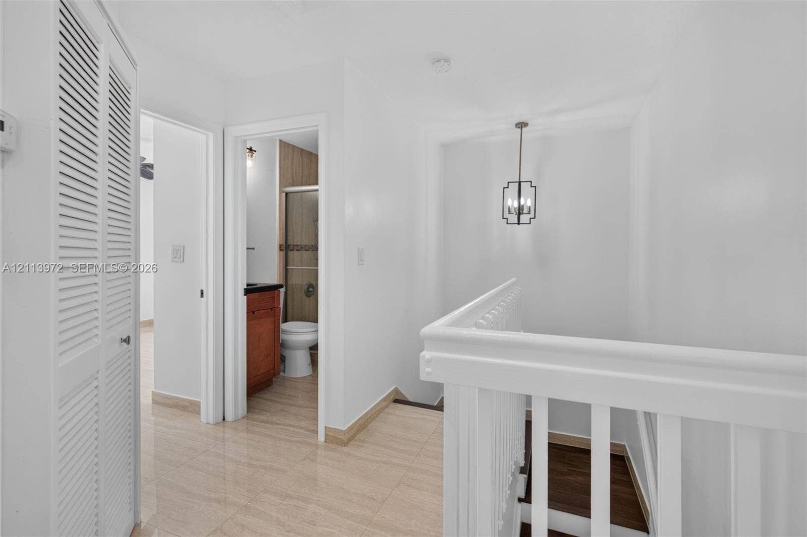 Louvered bi-fold closet doors, tile flooring, white-painted wooden railings, and a hanging geometric pendant light fixture
