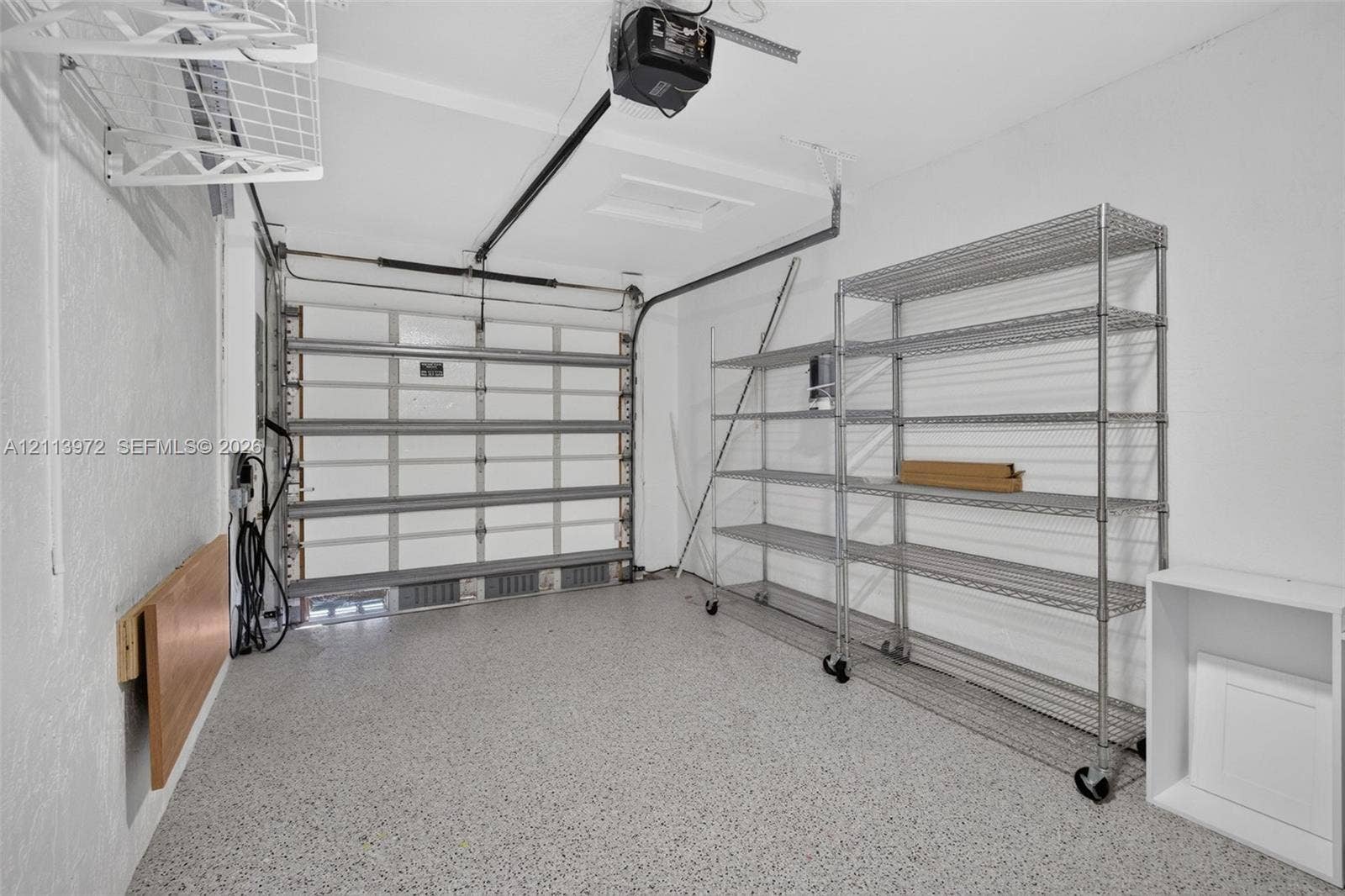 Garage featuring speckled epoxy flooring, ceiling-mounted automatic door opener, and wall-mounted metal wire shelving units