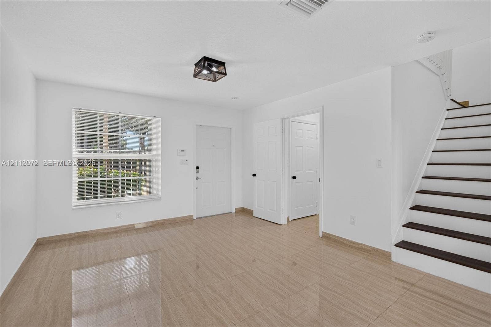 Neutral-tone tile flooring, multi-pane window, flush-mount geometric ceiling light, and staircase with dark wood-finish treads