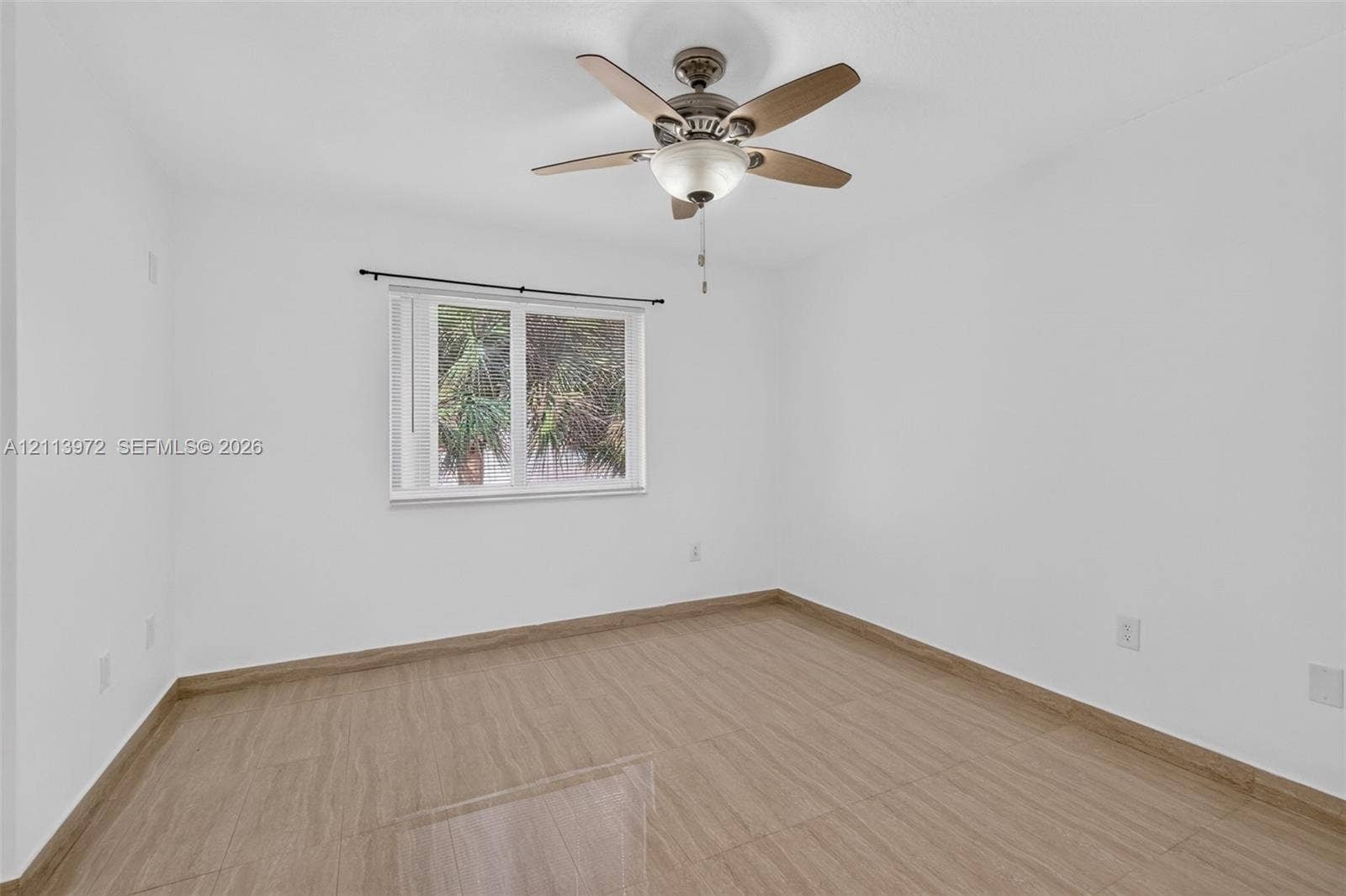 Interior room featuring wood-finish flooring, a multi-blade ceiling fan with integrated lighting, and a window with a curtain rod