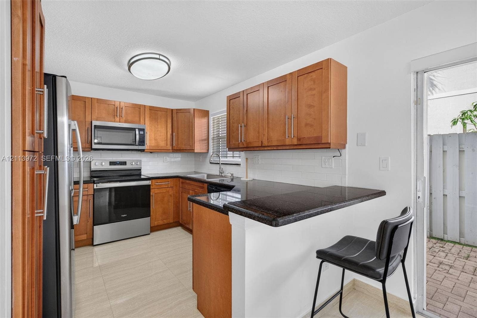 Kitchen featuring wood cabinetry, dark stone-finish countertops, stainless steel appliances, a white subway tile backsplash, and tile flooring